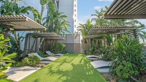 Ein gepflegter Garten mit einem zentralen Rasen, umgeben von verschiedenen tropischen Pflanzen und hölzernen Pergolen.