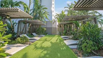 A well-maintained garden with a central lawn, surrounded by various tropical plants and wooden pergolas.
