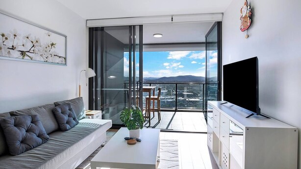 Ein modernes Wohnzimmer mit einer Couch, einem Couchtisch, einem Fernseher und einem Balkon mit Blick auf die Stadt.
