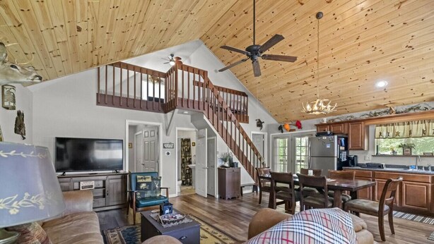 A spacious living area with a wooden ceiling, a staircase, a television, and a kitchen area. - Hocking Hills Half Stoned Cabin in the Woods (Nelsonville)