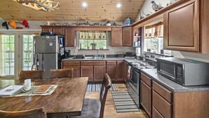 A kitchen with wooden cabinets, a dining table, and a chandelier. - Hocking Hills Half Stoned Cabin in the Woods (Nelsonville)