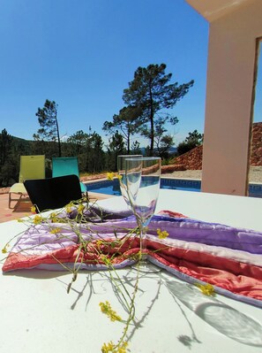 Ein Tisch mit einem Glas Wasser, einem Tuch und einer Pflanze. Im Hintergrund sind Stühle und ein Pool zu sehen.