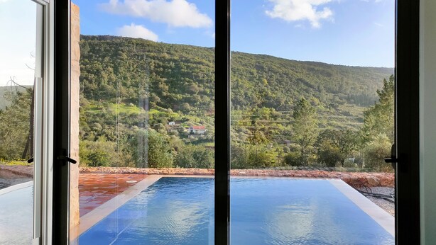 Udsigt gennem en dør til en swimmingpool med et bjerglandskab i baggrunden.