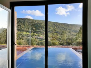 Blick durch eine Tür auf ein Schwimmbecken mit einer Berglandschaft im Hintergrund.
