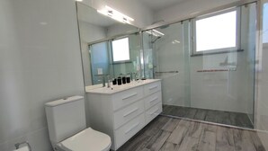 Et moderne badeværelse med toilet, vaskebord med spejl og en bruseniche med glasvægge.