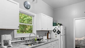 Cocina compacta con armarios blancos, encimera de granito, cafetera, lavamanos y refrigerador.