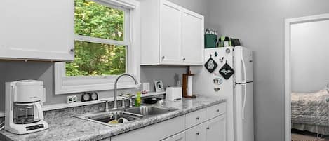 A compact kitchen with white cabinets, a granite countertop, a coffee maker, a sink, and a refrigerator.
