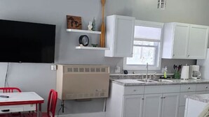 Una cocina moderna con armarios blancos, ventilador de techo, una mesa de comedor con sillas rojas y una mecedora de madera.