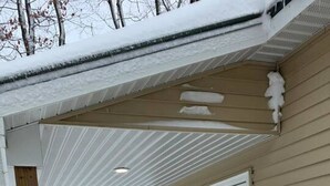 Un espacio exterior cubierto de nieve, con un poste de madera, una escalera apoyada en una puerta y el suelo cubierto de nieve.