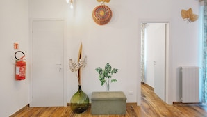 A hallway with a white door, a fire extinguisher, a green vase, a plant, and a grey bench. - Room 'Green Roof Palermo - 3 Rosmarino' with Balcony, Wi-Fi and Air Conditioning (Palermo)