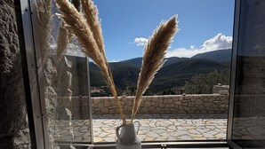 A window with a vase of pampas grass, a stone wall, and a view of mountains. - Villa ELIA HOUSE near Nafplio sea and mountain view (Nauplie)