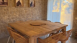 A rustic dining area with a wooden table, wicker chairs, stone walls, and framed artwork. - Villa ELIA HOUSE near Nafplio sea and mountain view (Nauplie)