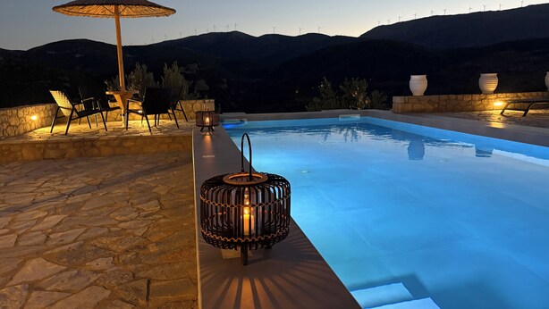A swimming pool with stone flooring, a lounge area with chairs and an umbrella, and a decorative lantern. - Villa ELIA HOUSE near Nafplio sea and mountain view (Nauplie)