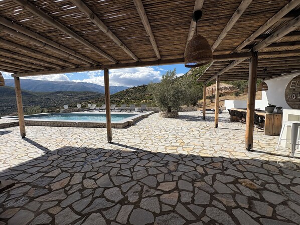 A stone-tiled patio with a pool, outdoor seating, and a view of mountains.