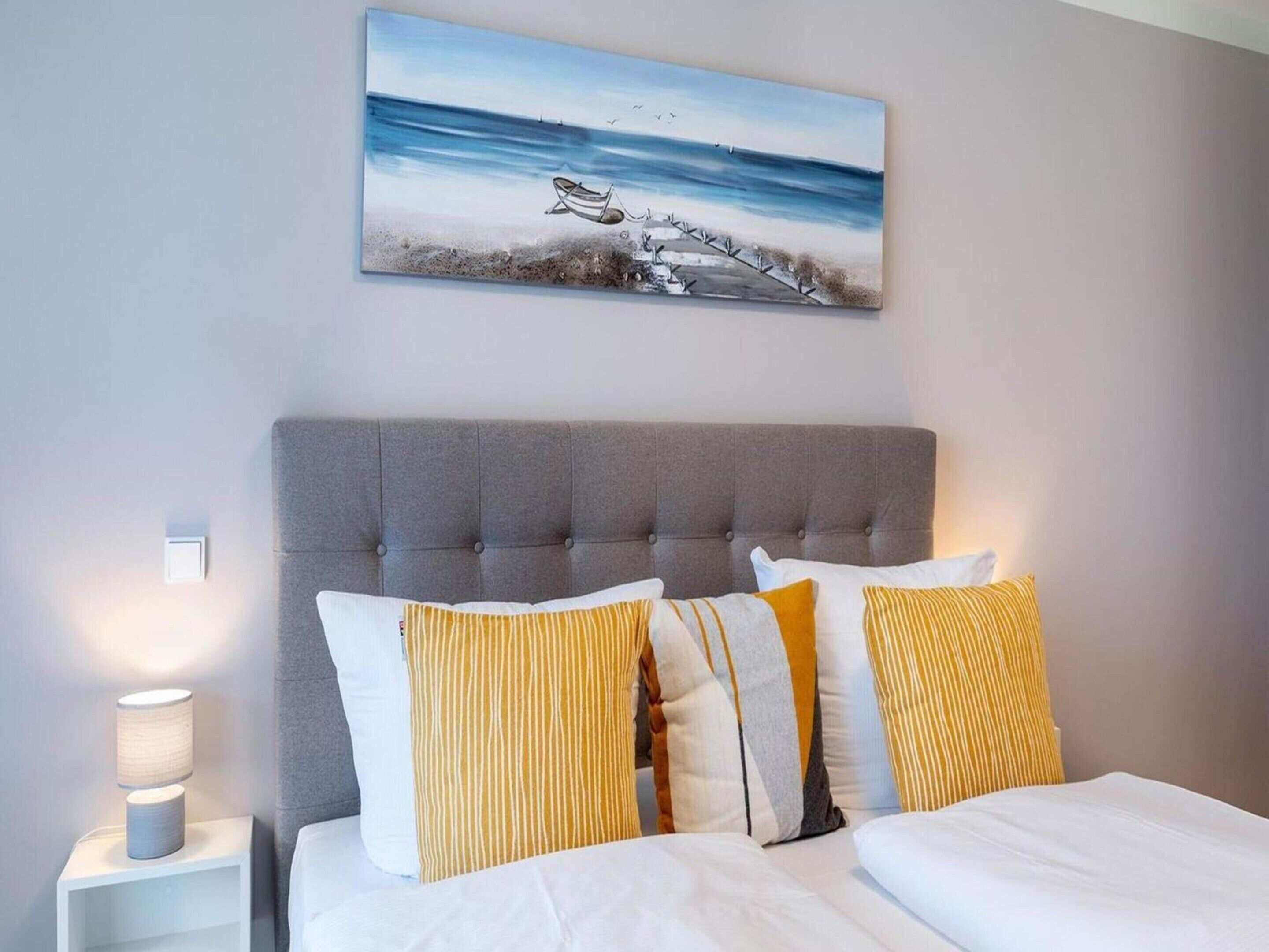 A bedroom with a grey upholstered headboard, white bedding, and striped pillows.