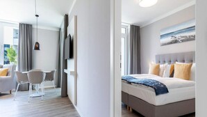A modern hotel room with a bed, a TV, a seating area with chairs, and a painting on the wall. - 4 Star Holiday Home in Travemunde (Lübeck)