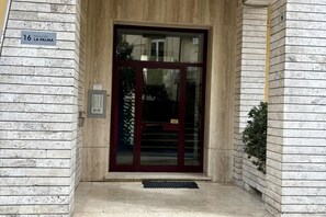 Ingresso di un edificio con facciata in marmo, una targa con un numero e una porta in vetro.