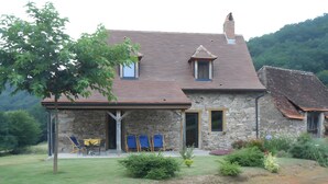 Ein Steinhaus mit überdachter Terrasse, Sitzgelegenheiten im Freien und Blick auf die umliegende Landschaft.