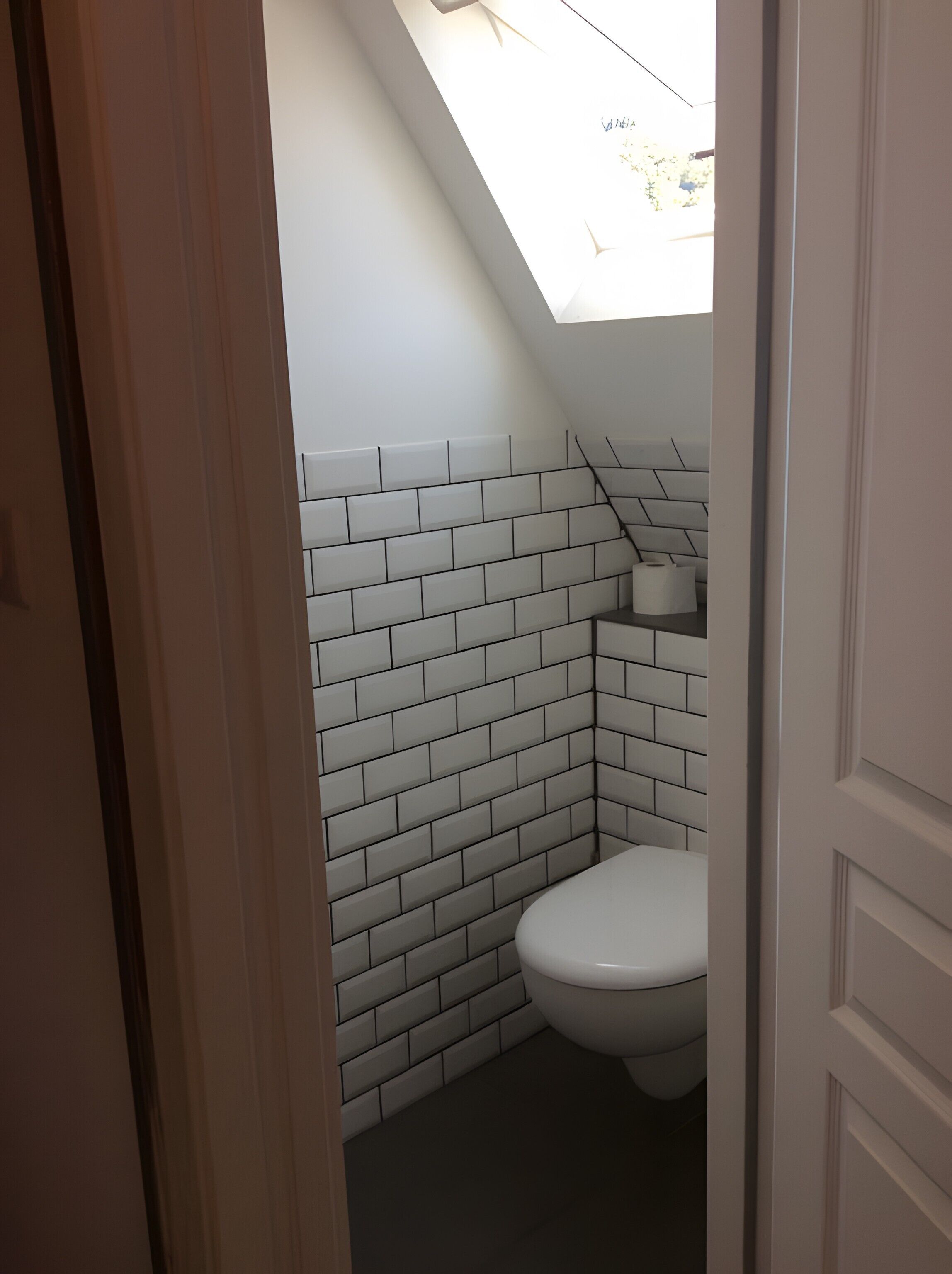 A small, narrow bathroom with white tiled walls and a white toilet.