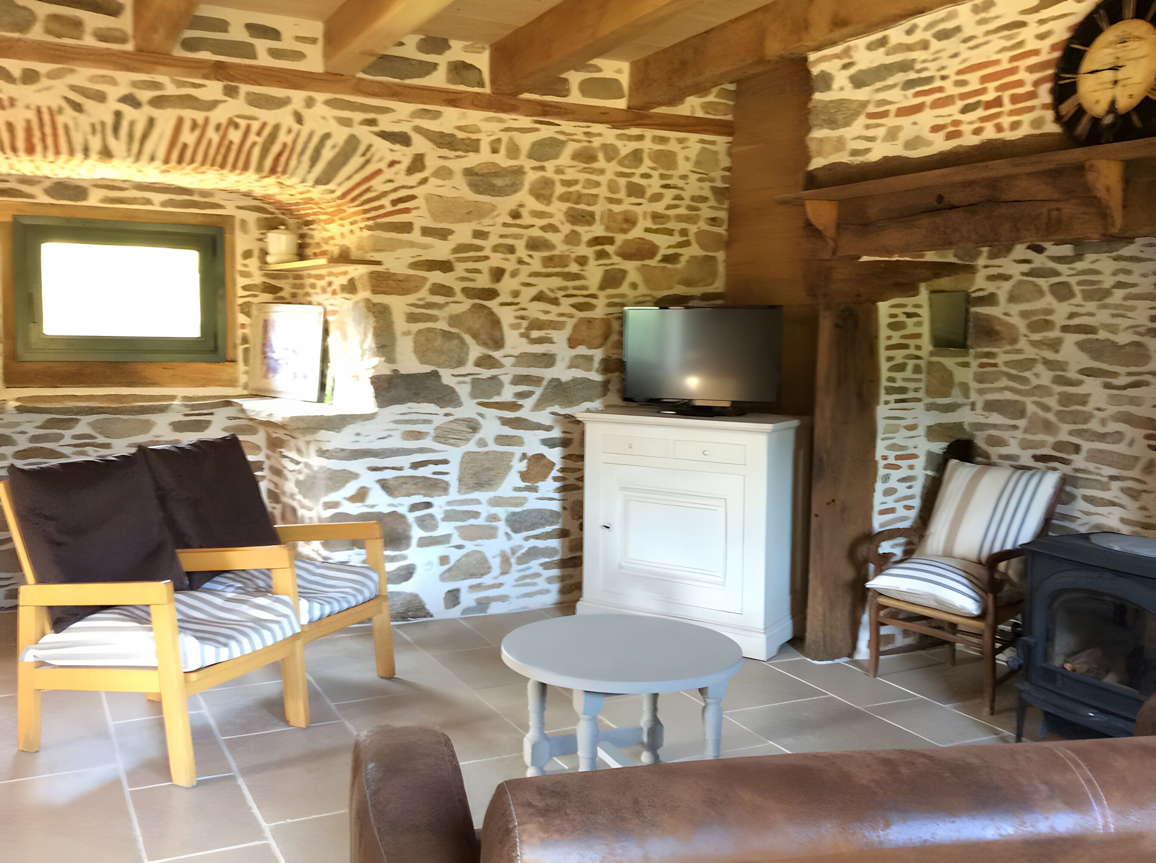 Une pièce aux murs de pierre, avec un téléviseur posé sur un meuble, une cheminée, un canapé et un fauteuil.