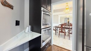 A kitchen with a white countertop, black cabinets, stainless steel appliances, and a dining area with wooden chairs and a chandelier. - Spacious 4 bd Modern Home with Private Yard & Games (Woodbridge)