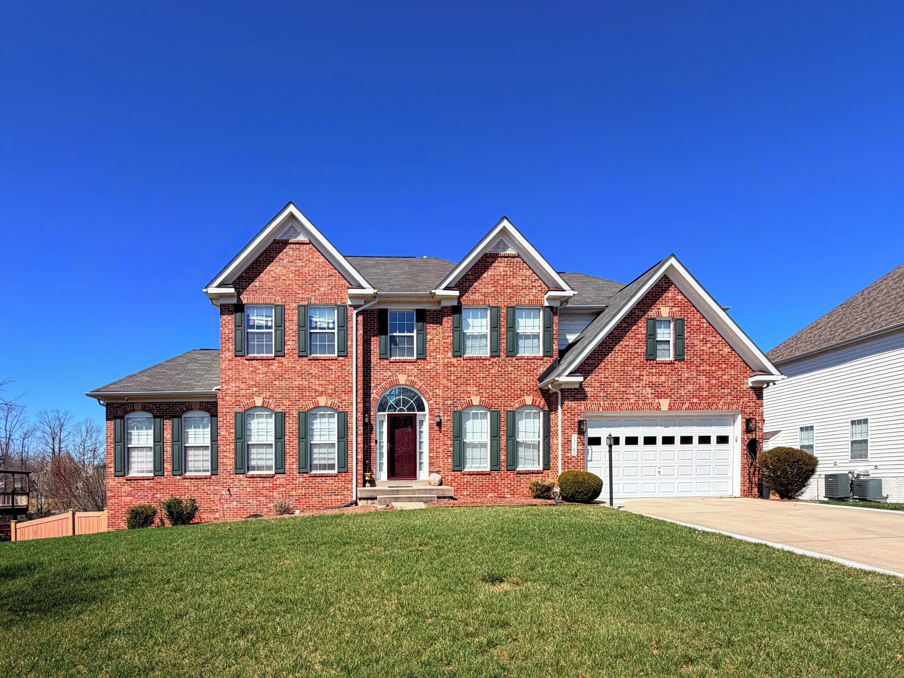 A two-story brick house with a red door, multiple windows, and a garage.