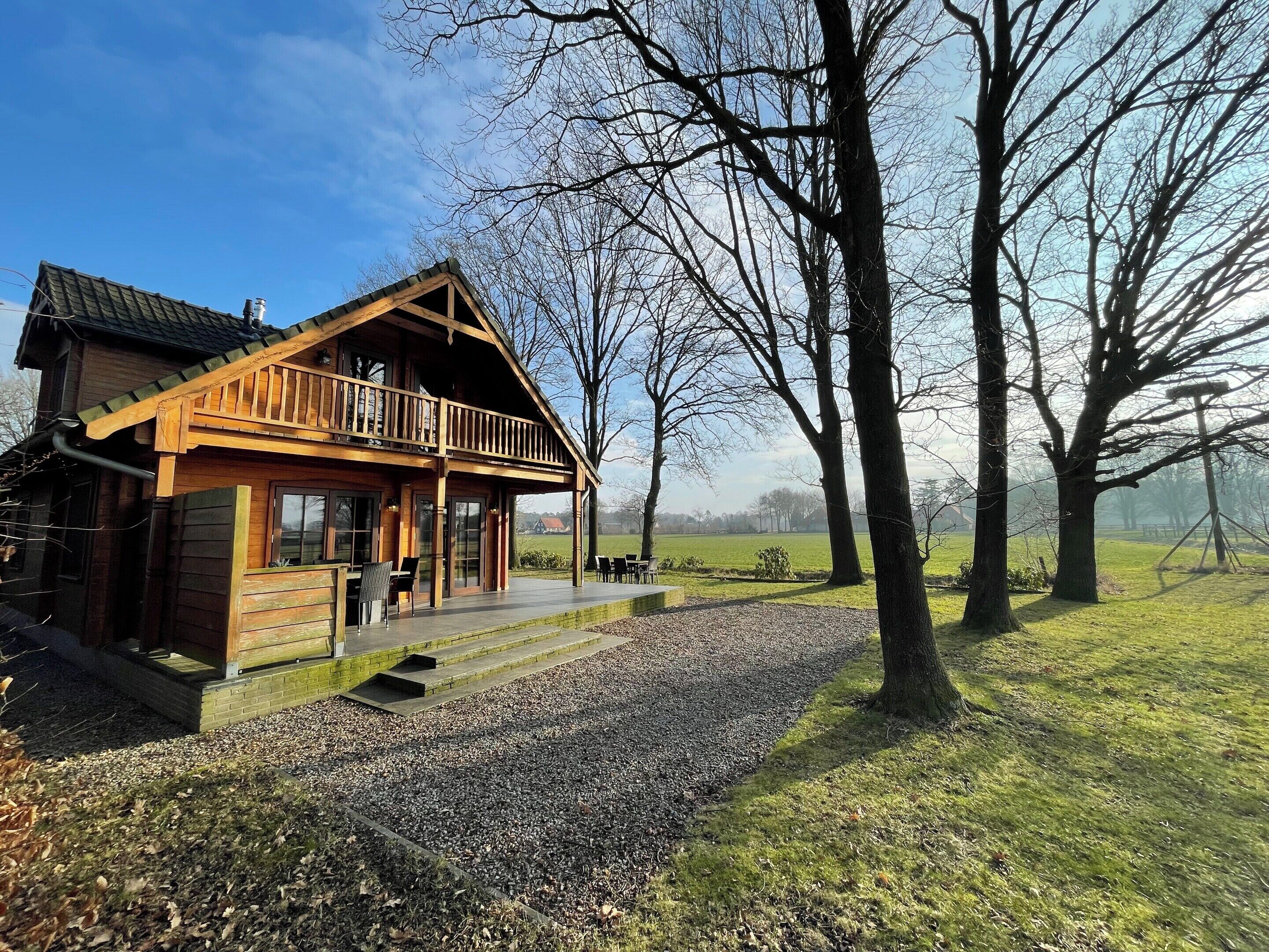 A wooden cabin with a balcony, a gravel path, and trees in the background.