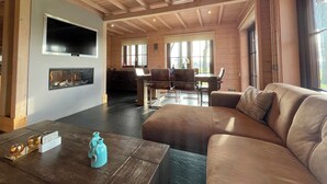 A living room with a fireplace, a sofa, a dining area, and a kitchen in the background. - Villa With Sauna & Tub (Den Ham)