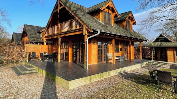 A wooden cabin with a porch, outdoor seating, and a gravel driveway. - Villa With Sauna & Tub (Den Ham)