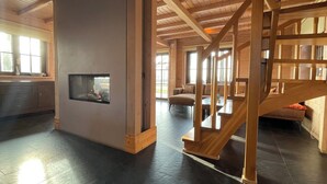 A spacious room with a wooden staircase, a fireplace, and large windows. - Villa With Sauna & Tub (Den Ham)