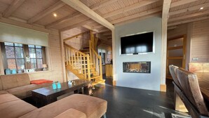 A spacious living area with a sofa, a coffee table, a fireplace, a TV mounted on the wall, and a wooden staircase. - Villa With Sauna & Tub (Den Ham)
