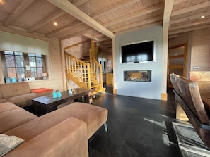 Ein großzügiger Wohnbereich mit Sofa, Couchtisch, Kamin, an der Wand montiertem Fernseher und einer Holztreppe.