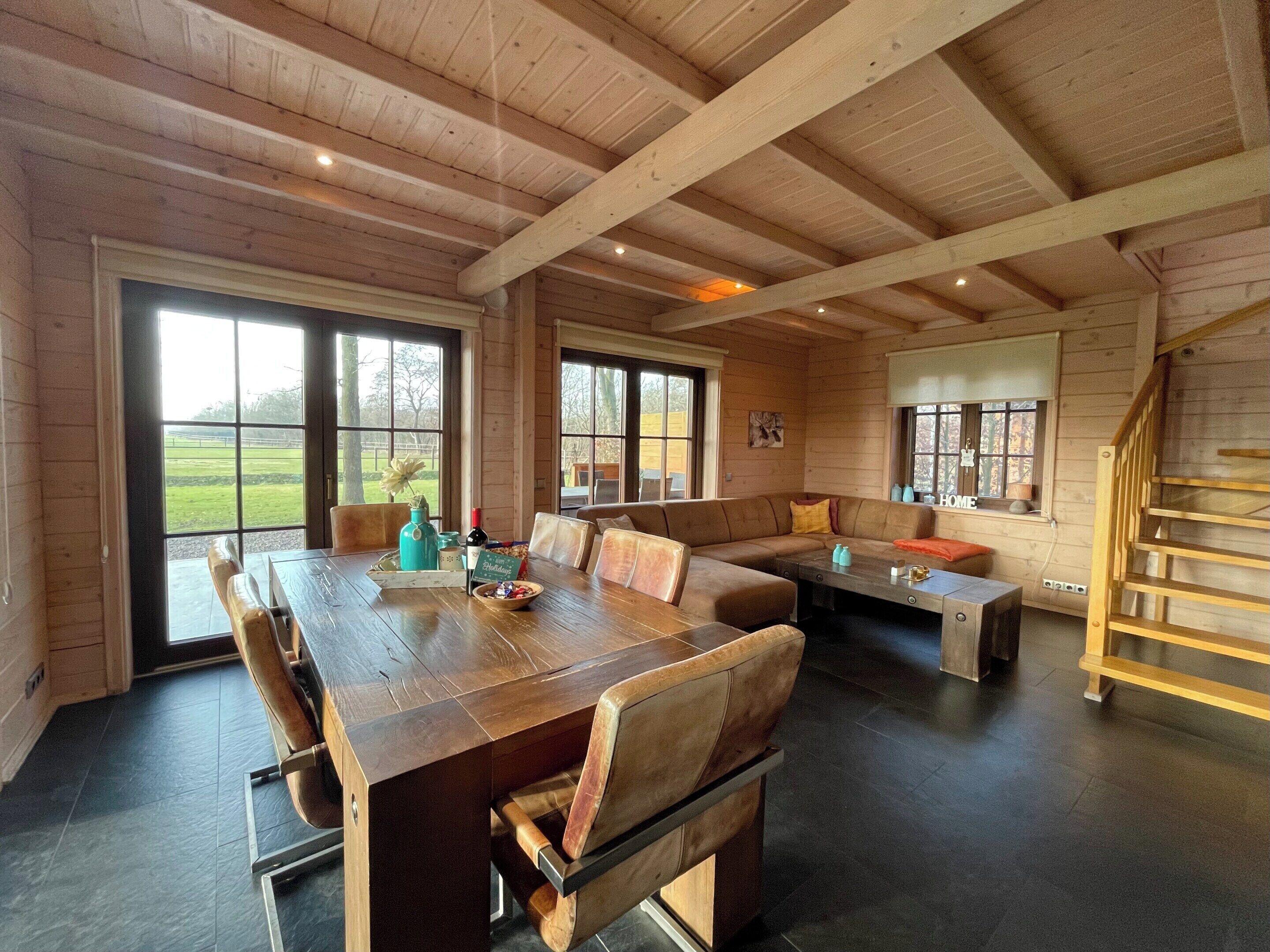 A spacious room with a wooden ceiling, large windows, a dining table, and a built-in bench.