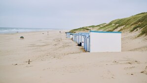 A beach with a row of blue and white beach huts along the shore. - Country Holiday Home for 6 Guests (Den Burg)