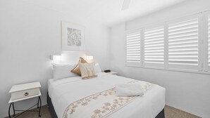 A bedroom with a bed, bedside table, lamp, and window with blinds. - Look at the beach, Alexandra Headland, sleeps 5 (Alexandra Headland)