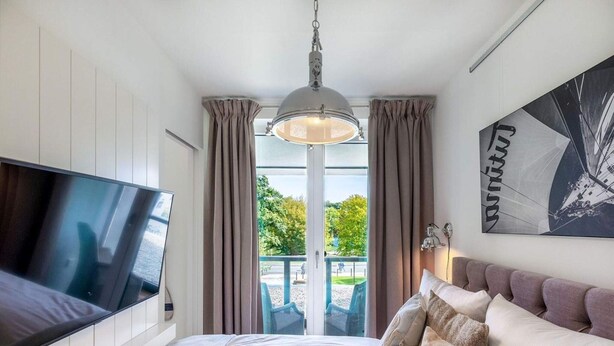 A bedroom with a bed, a TV, a ceiling light, a window with curtains, and a wall-mounted artwork. - 4 Star Holiday Home in Travemunde (Lübeck)