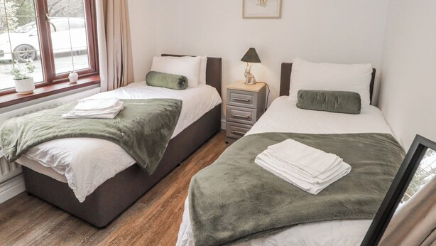 Una habitación con dos camas, una mesita de noche con lámpara, un cuadro enmarcado en la pared y una ventana con cortinas.