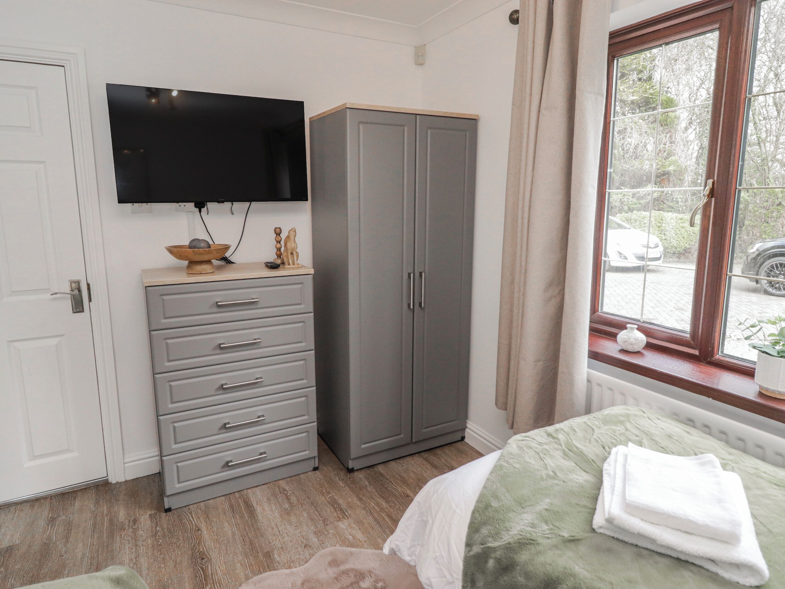 A bedroom with a bed, a wardrobe, a television, and a window with a view of the outside.