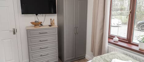 Un dormitorio con cama, armario, televisor y ventana con vistas al exterior.