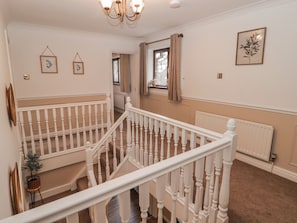 Una escalera con balaustres blancos, un candelabro y cuadros en las paredes.