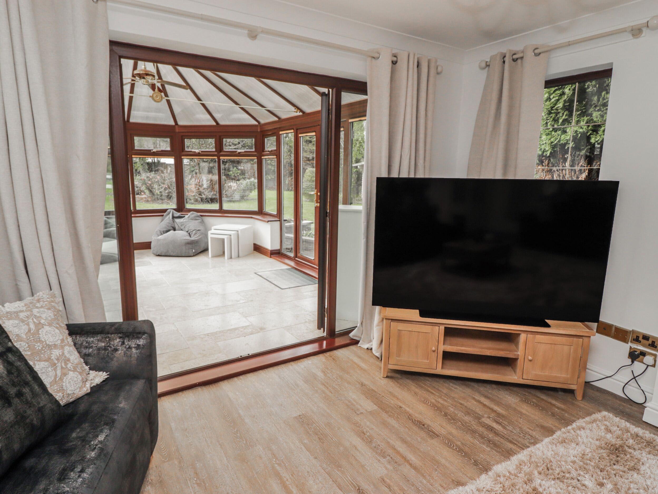 A living room with a TV on a wooden stand, a sofa, a glass door leading outside, and a view of the outdoors.