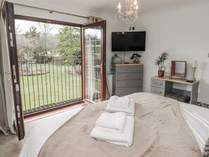 Un dormitorio con cama, televisor, escritorio con espejo y vista a un jardín por un ventanal corredera.