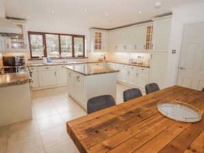 A spacious kitchen with white cabinetry, a wooden dining table, and a large window. - Willows Lodge at Carreg Llwyd (Cardiff)