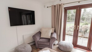 Una sala de estar moderna con un sofá, un televisor de pantalla plana, una puerta corrediza de vidrio y un reposapiés redondo.