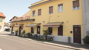 Un edificio giallo con molte finestre, una porta e area esterna con tavoli e sedie.