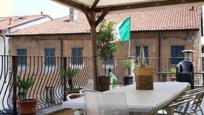 Una veranda coperta all'aperto con tavolo e sedie, piante in vaso e vista sugli edifici sullo sfondo.