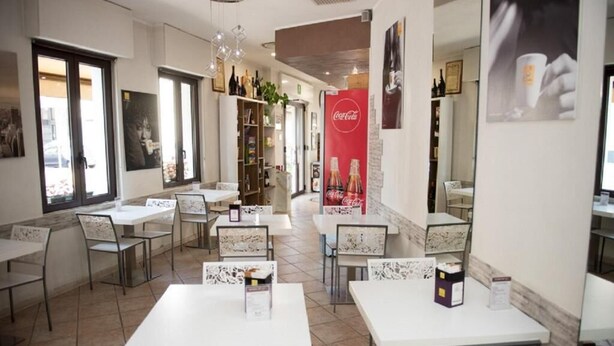 Un ristorante con tavoli e sedie bianche, un cartello Coca-Cola e una libreria con diversi oggetti.