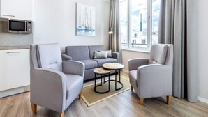 A modern living room with a grey sofa, two armchairs, a small coffee table, and a kitchen area with a microwave. - 4 Star Holiday Home in Travemunde (Lübeck)