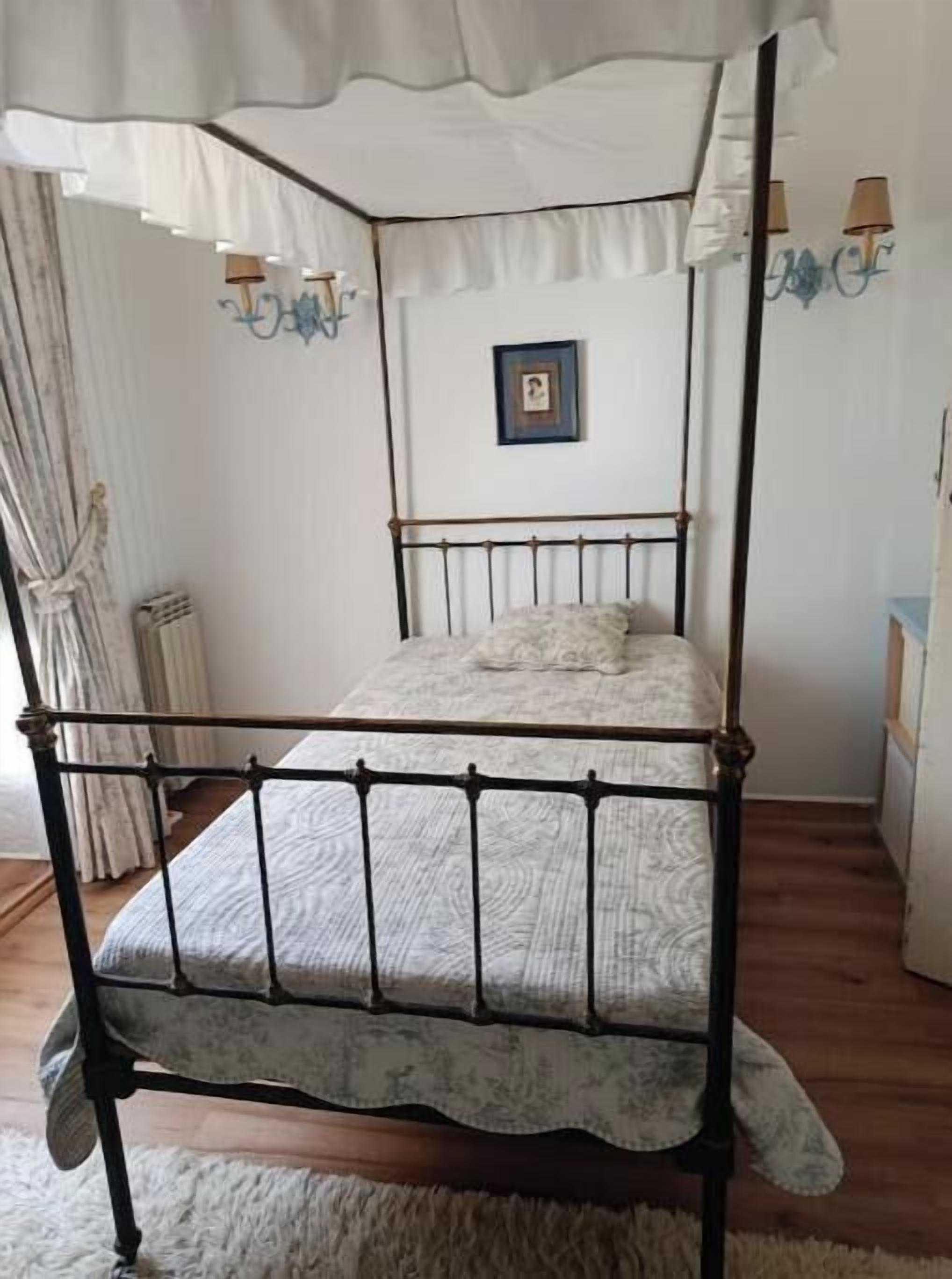 Een bed met hemel, een ingelijst kunstwerk aan de muur en een nachtkastje met een lamp.