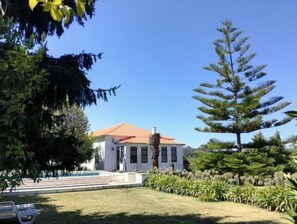 Ein zweistöckiges Gebäude mit rotem Dach, umgeben von einem gepflegten Garten mit verschiedenen Pflanzen und einem Swimmingpool.